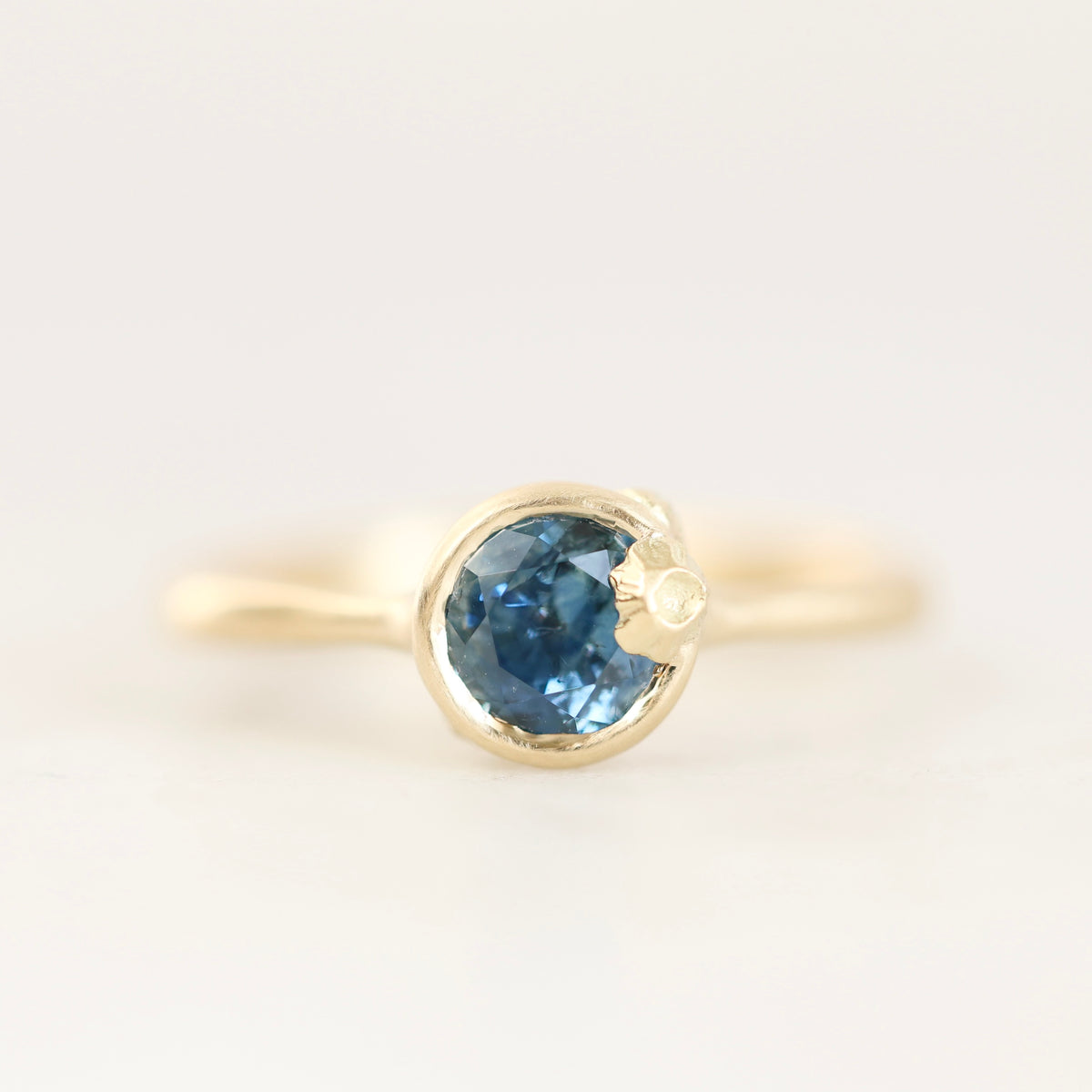 A yellow gold ring featuring a round-cut blue gemstone in a bezel setting, shown against a plain white background.