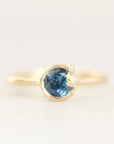 A yellow gold ring featuring a round-cut blue gemstone in a bezel setting, shown against a plain white background.