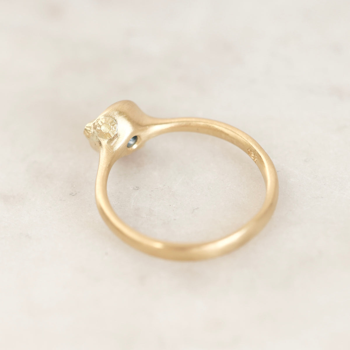 A gold ring with a unique curved shank and a small blue gemstone accent, photographed on a light marble surface.