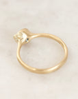 A gold ring with a unique curved shank and a small blue gemstone accent, photographed on a light marble surface.