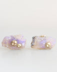 A pair of stud earrings featuring raw, iridescent opal pieces with a small gold barnacle accent on each, set against a plain white background.