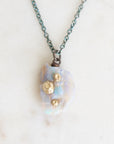 Fossilized opal pendant with gold barnacle details on an oxidized silver chain. Laying against marble background. 