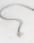 Fossilized opal pendant with gold barnacle details on an oxidized silver chain. Laying against marble background. 