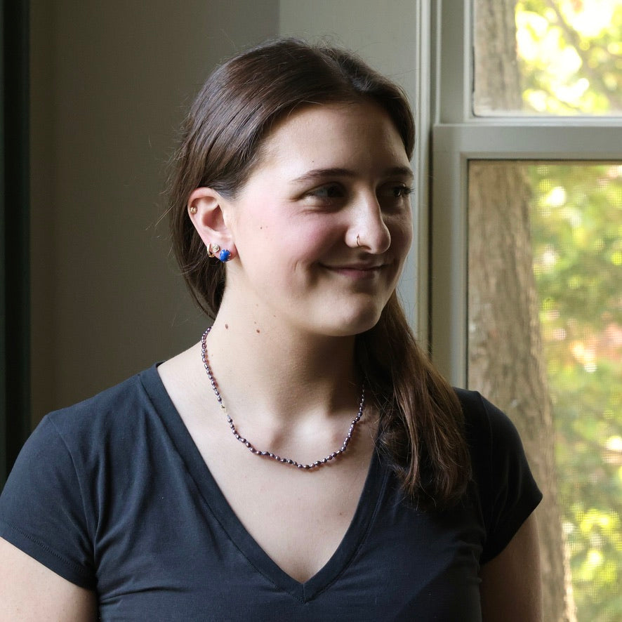 Woman wearing a necklace in front of a window with greenery outside