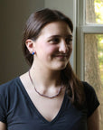 Woman wearing a necklace in front of a window with greenery outside