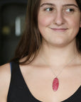 A woman wearing a silver chain necklace with a polished pink oval stone pendant, shown in a close-up portrait.