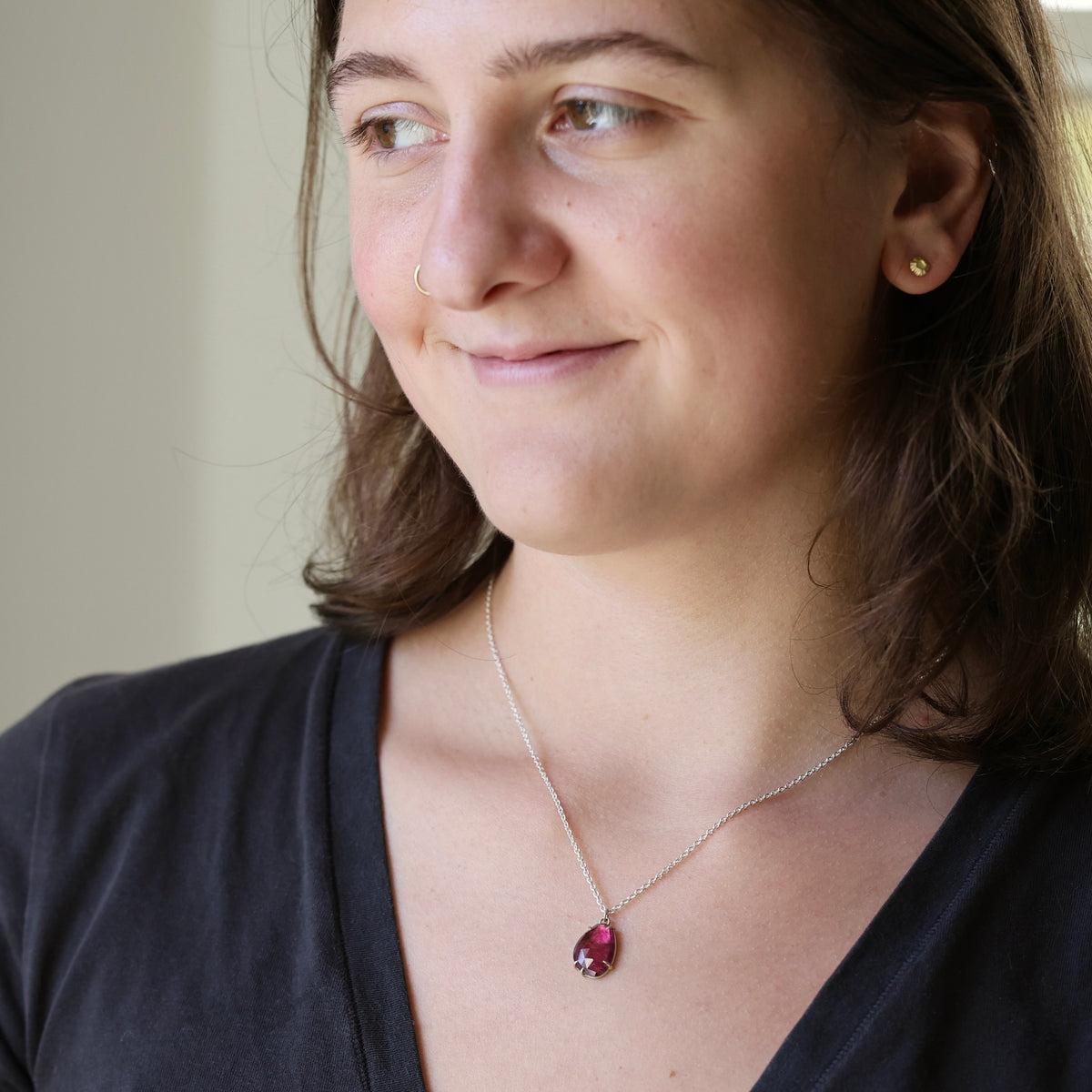 Woman wearing dark pink necklace against a neutral background