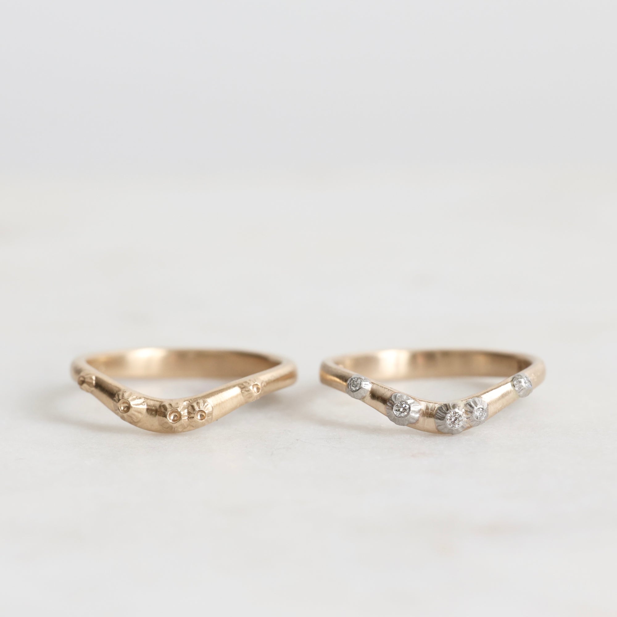 two gold curved rings, one with diamonds, on a light gray background