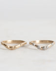 two gold curved rings, one with diamonds, on a light gray background