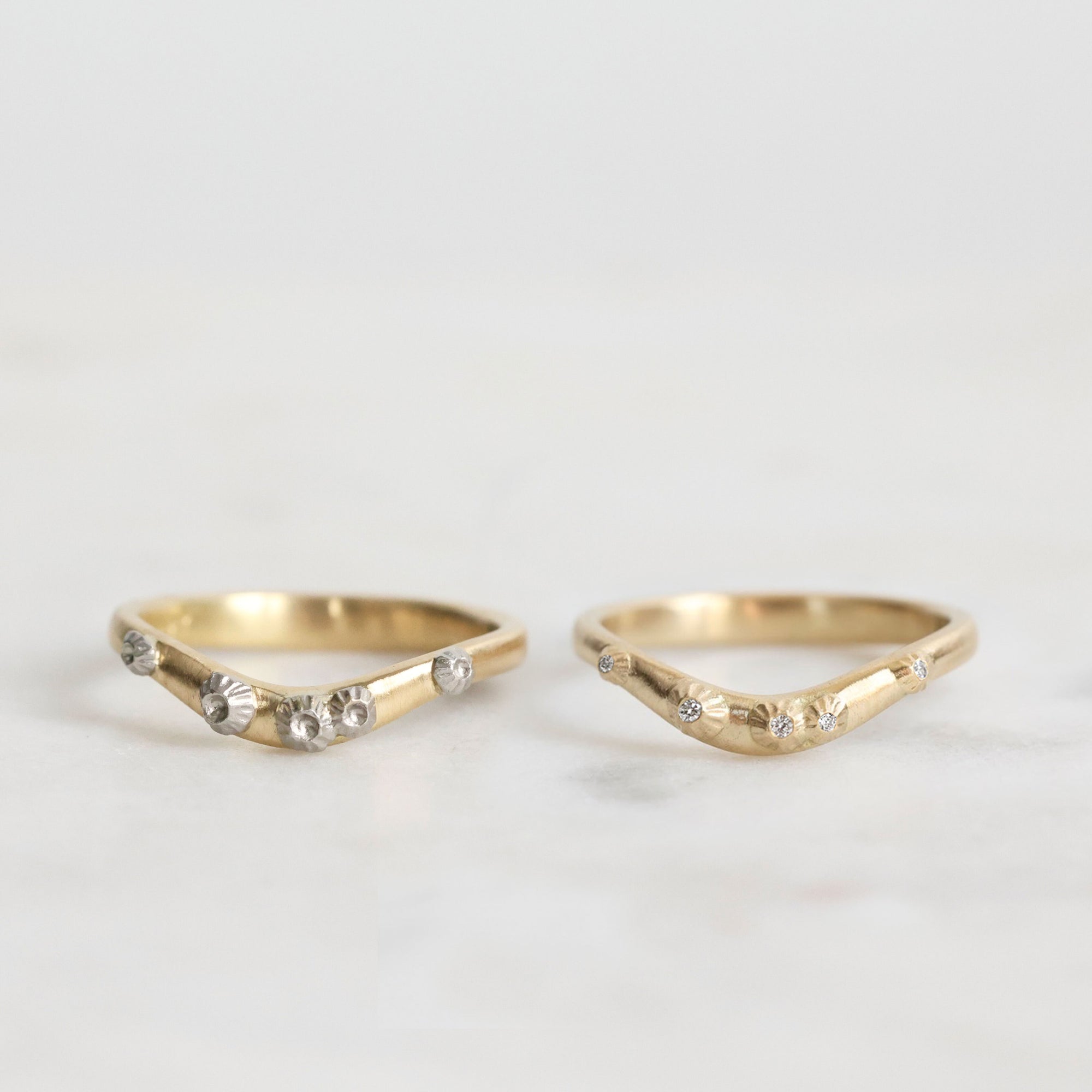 Two gold rings with small diamonds on a light gray background