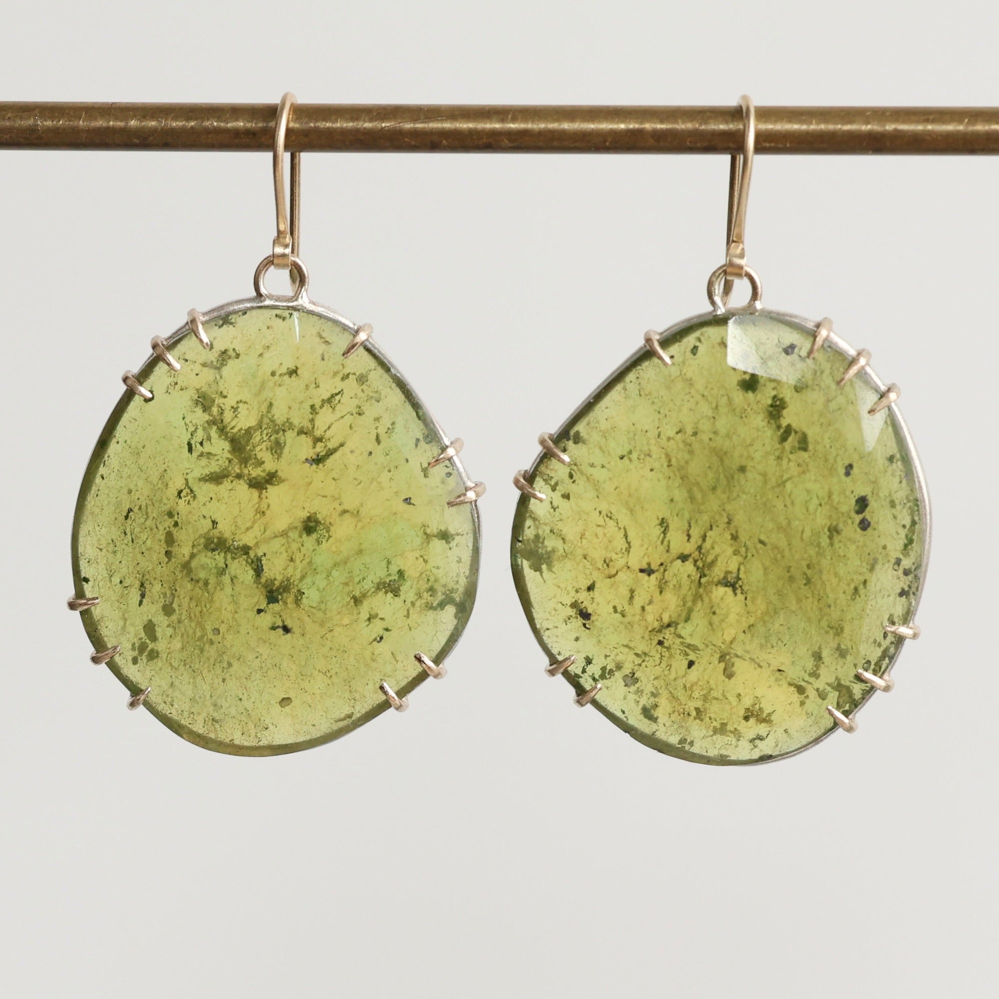 Green stone earrings on a thin rod against a light gray background
