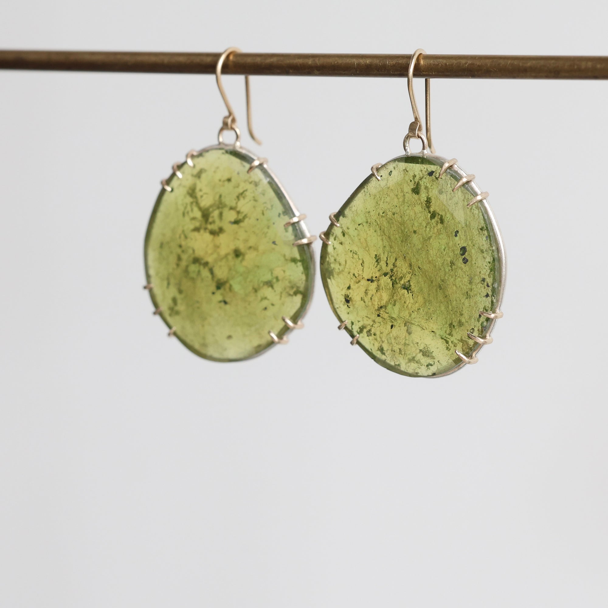 Green oval earrings with silver accents on a light gray background