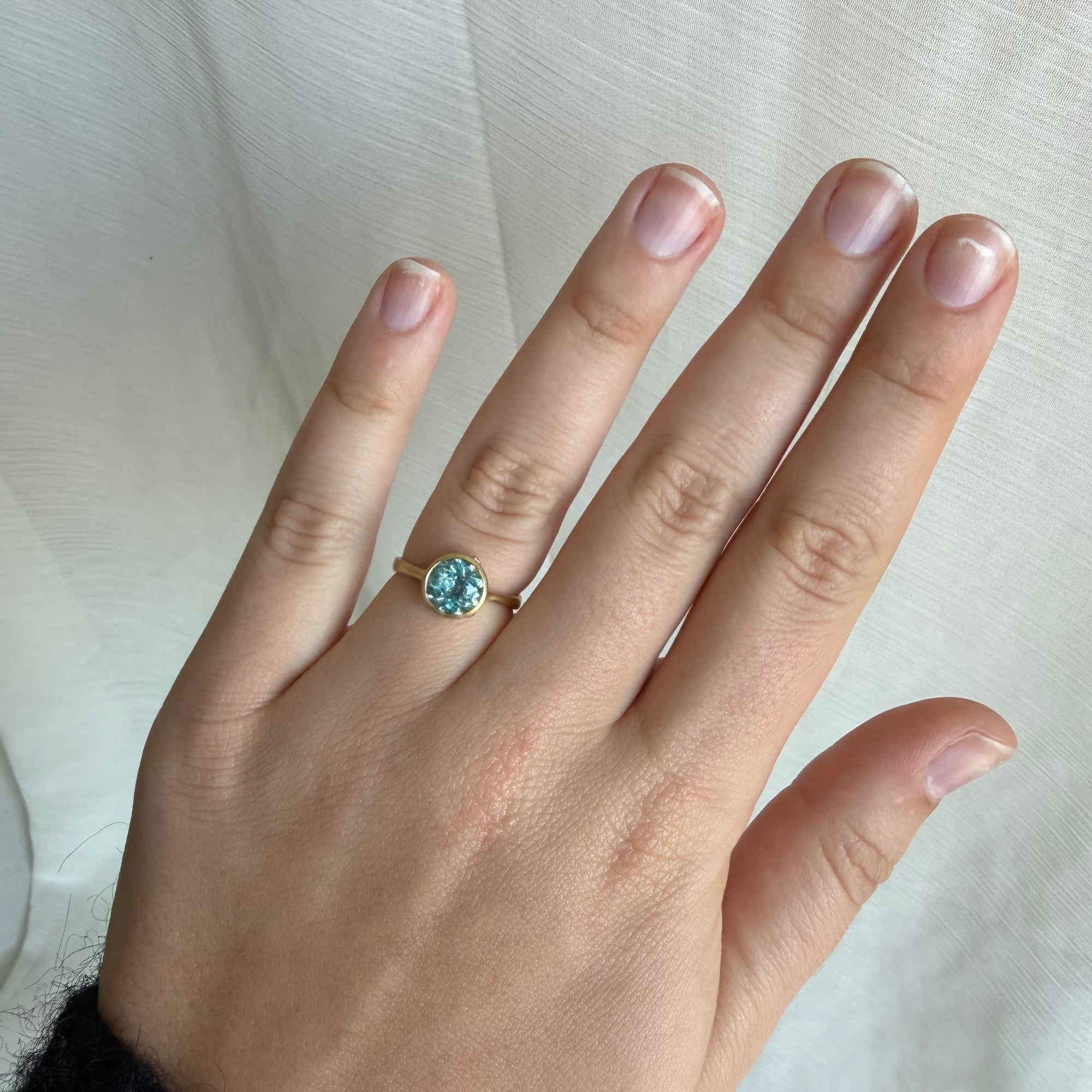 Hand wearing a ring with a blue gemstone on a light background