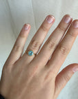 Hand wearing a ring with a blue gemstone on a light background