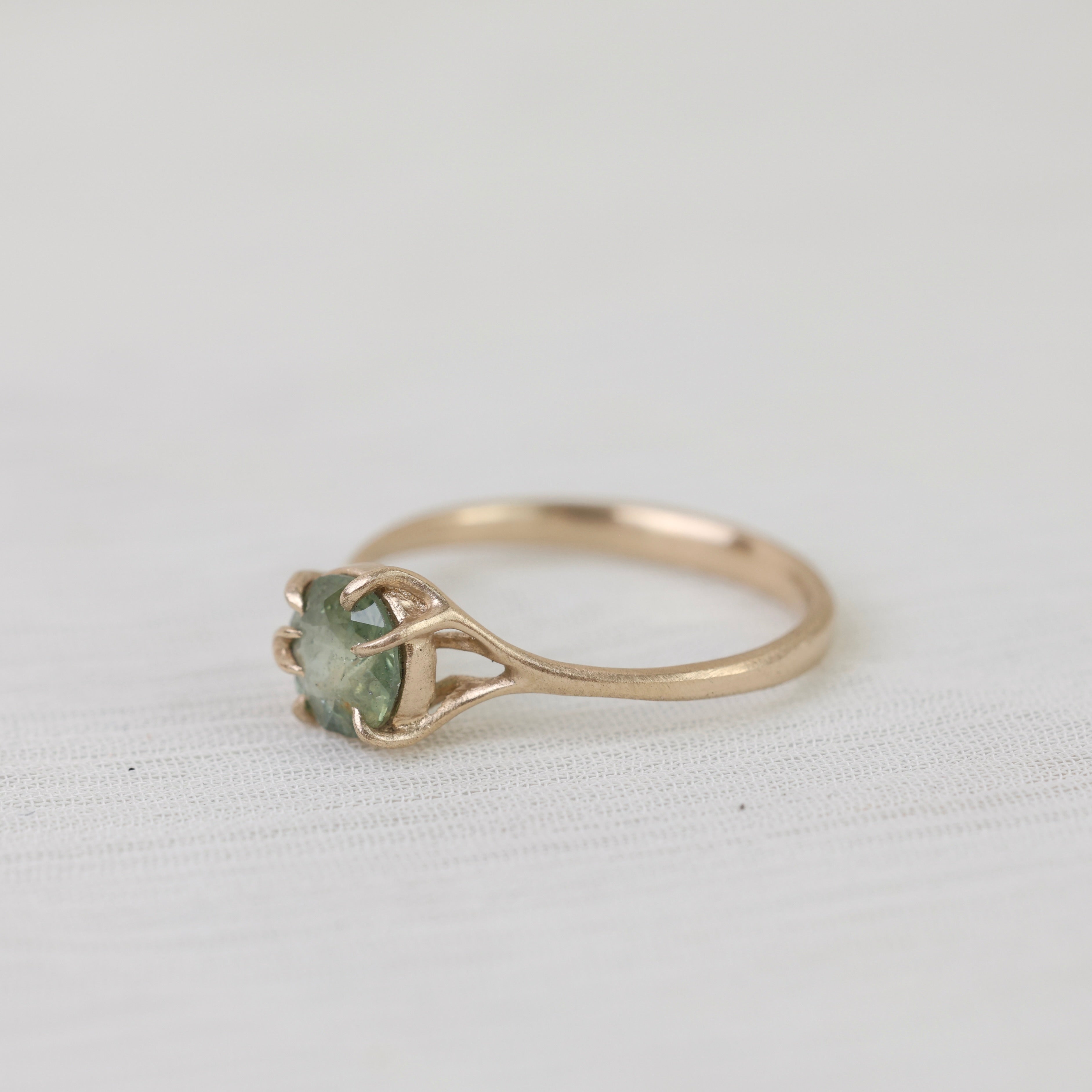 Gold ring with a green gemstone on a white fabric background
