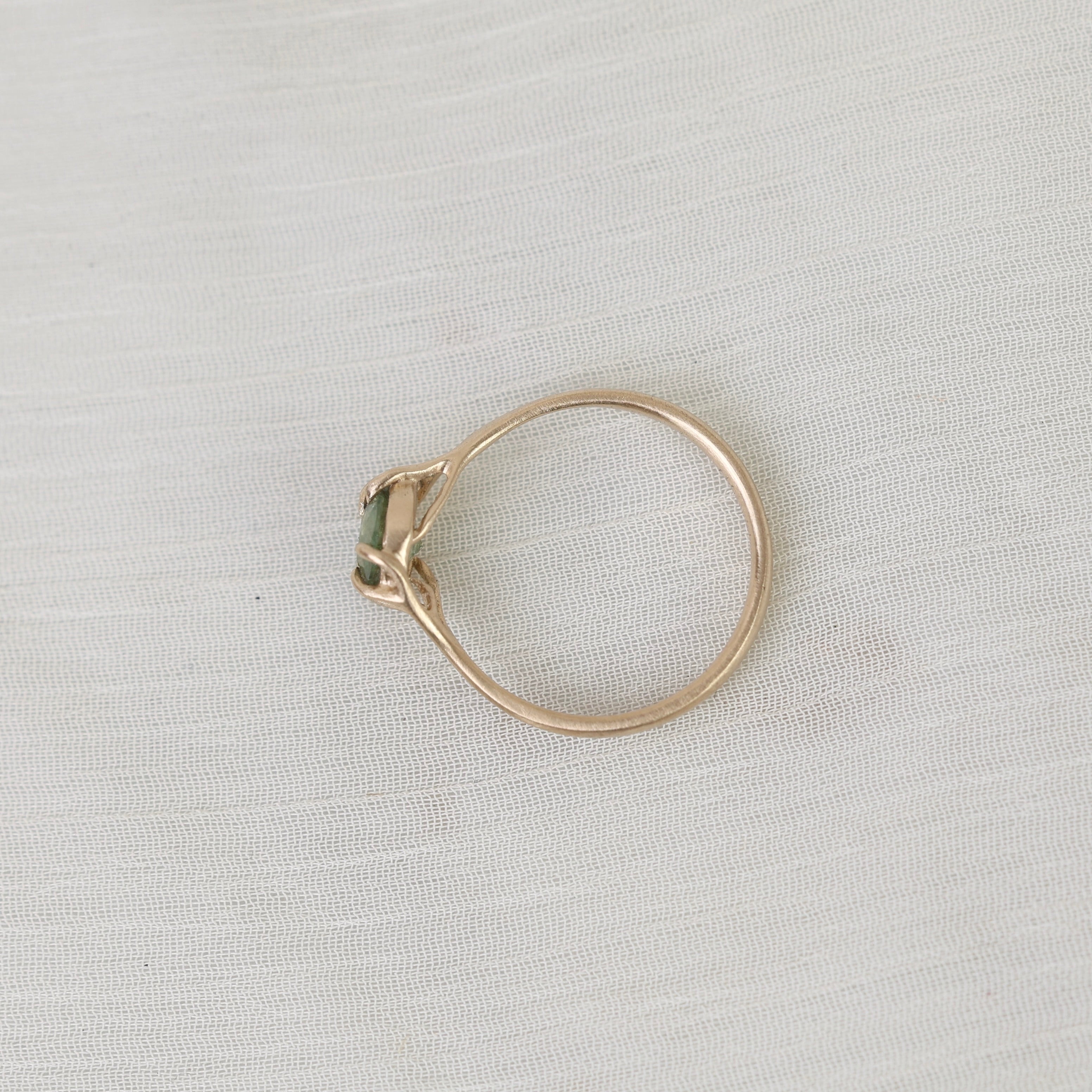 Gold ring with a green gemstone on a light gray fabric background