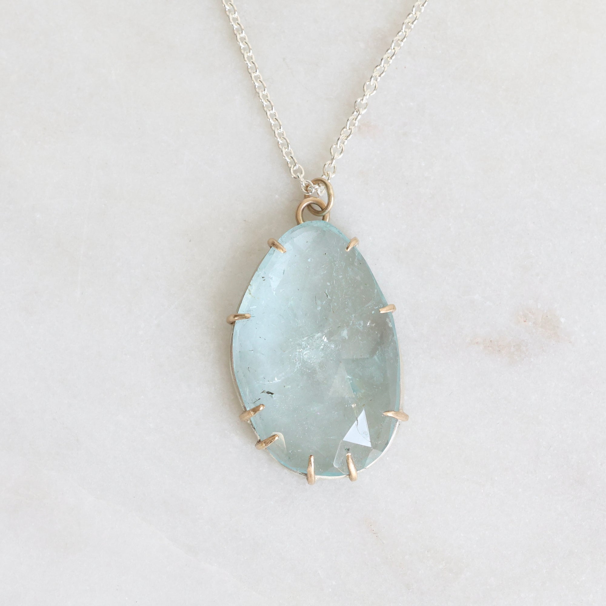 Necklace with a large teardrop-shaped green stone on a light gray background