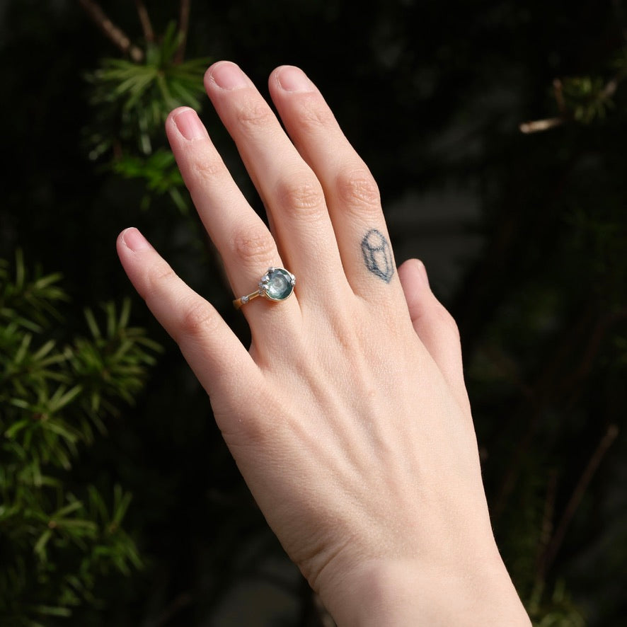 Large green sapphire ring with lots of barnacles on hand with tattoo against natural background 