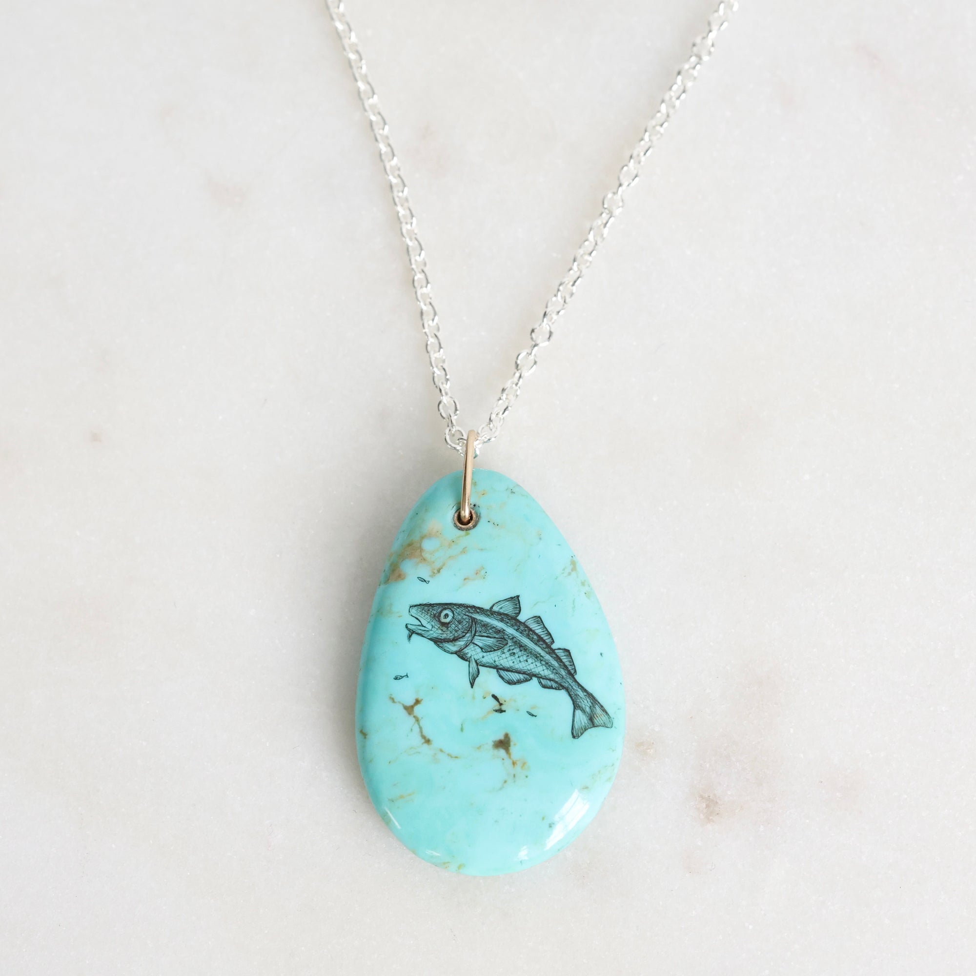 Turquoise pendant with fish design on a white background