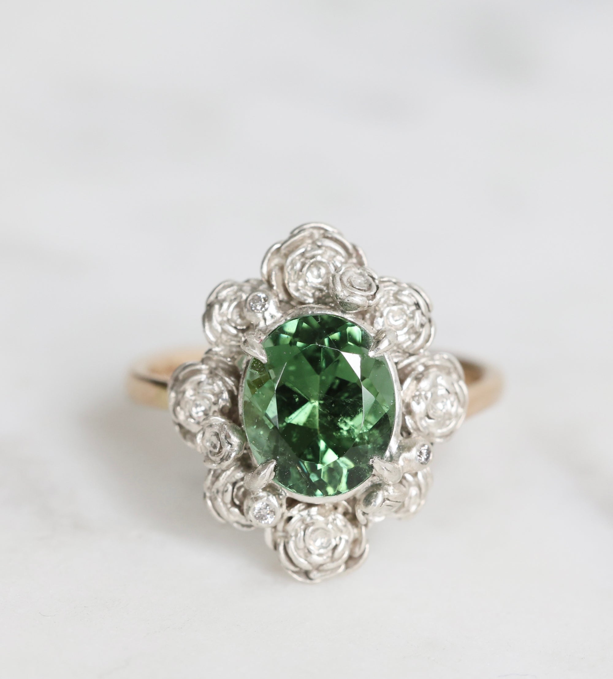 Ring with a green gemstone and diamond-studded band on a light gray background