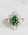 Ring with a green gemstone and diamond-studded band on a light gray background