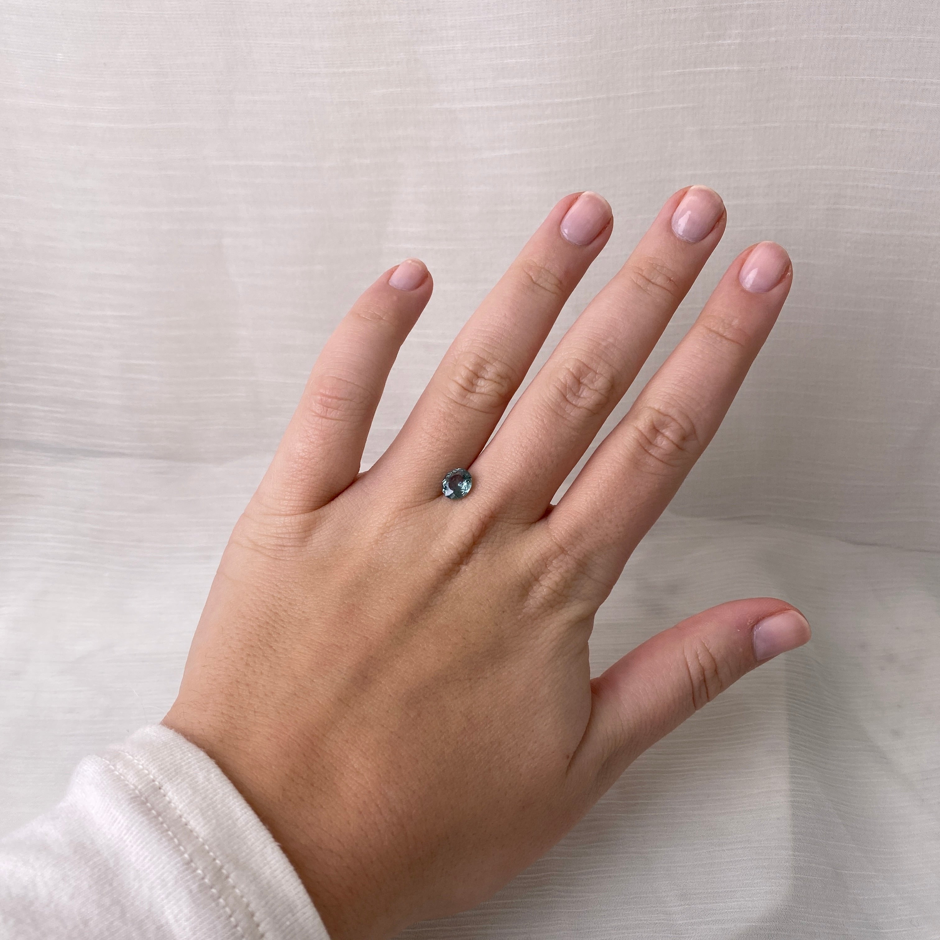 Hand wearing a ring with a green gemstone on a plain background