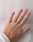 Hand wearing a ring with a green gemstone on a plain background