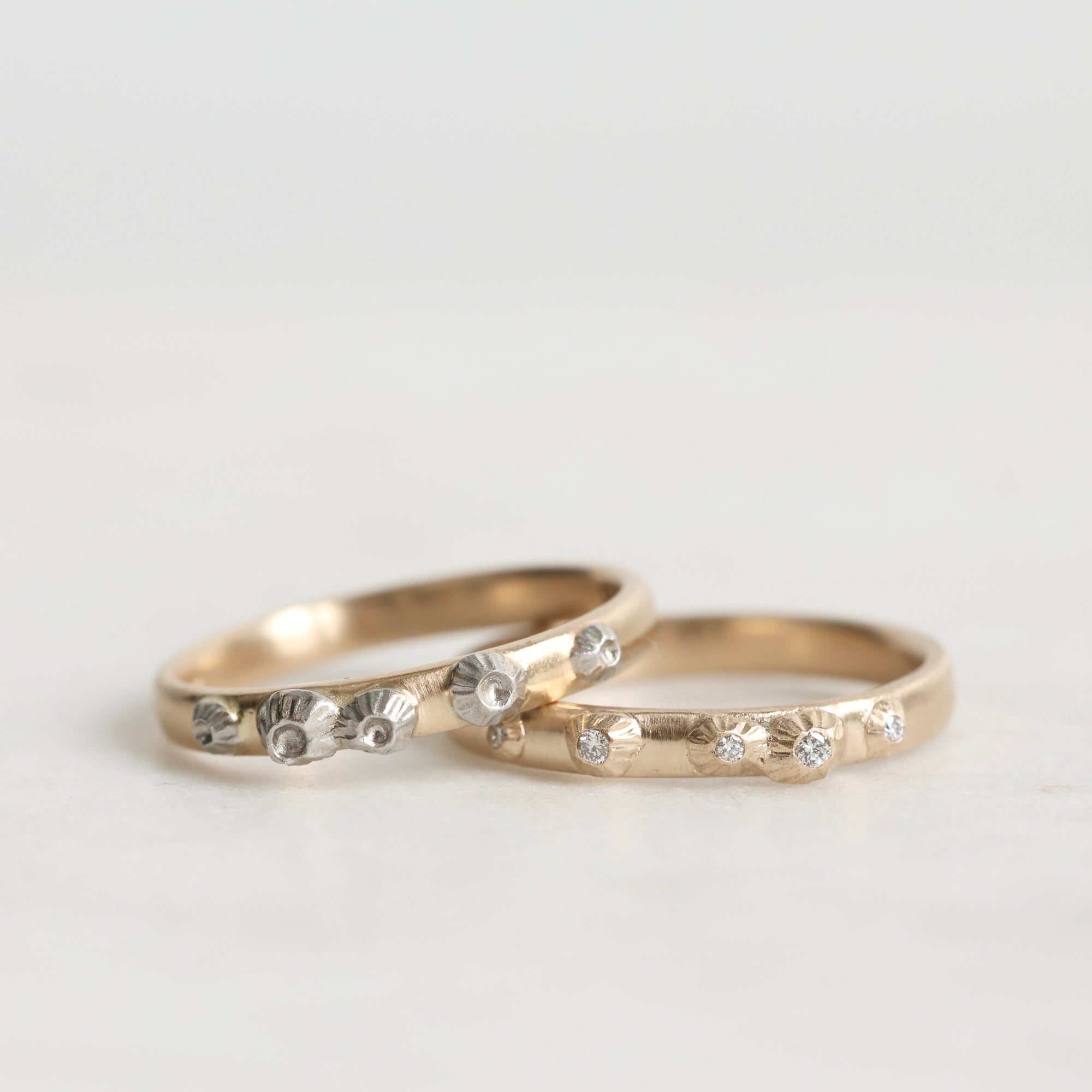 Two gold rings with diamond accents on a light gray background