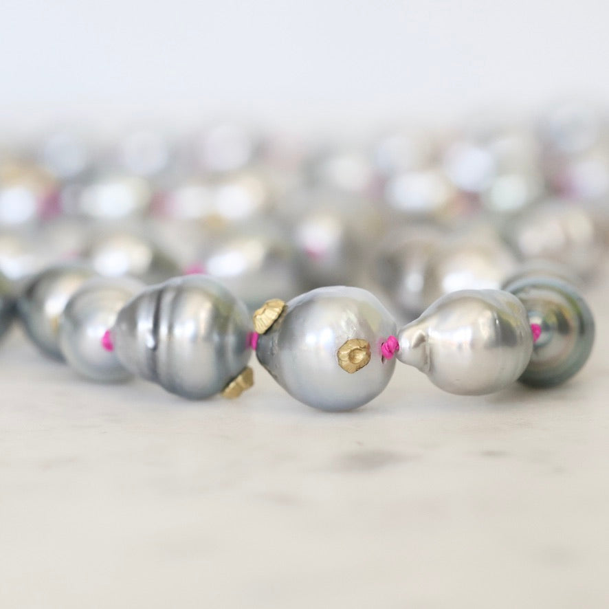 Close-up of a pearl necklace with gold and pink accents on a light background