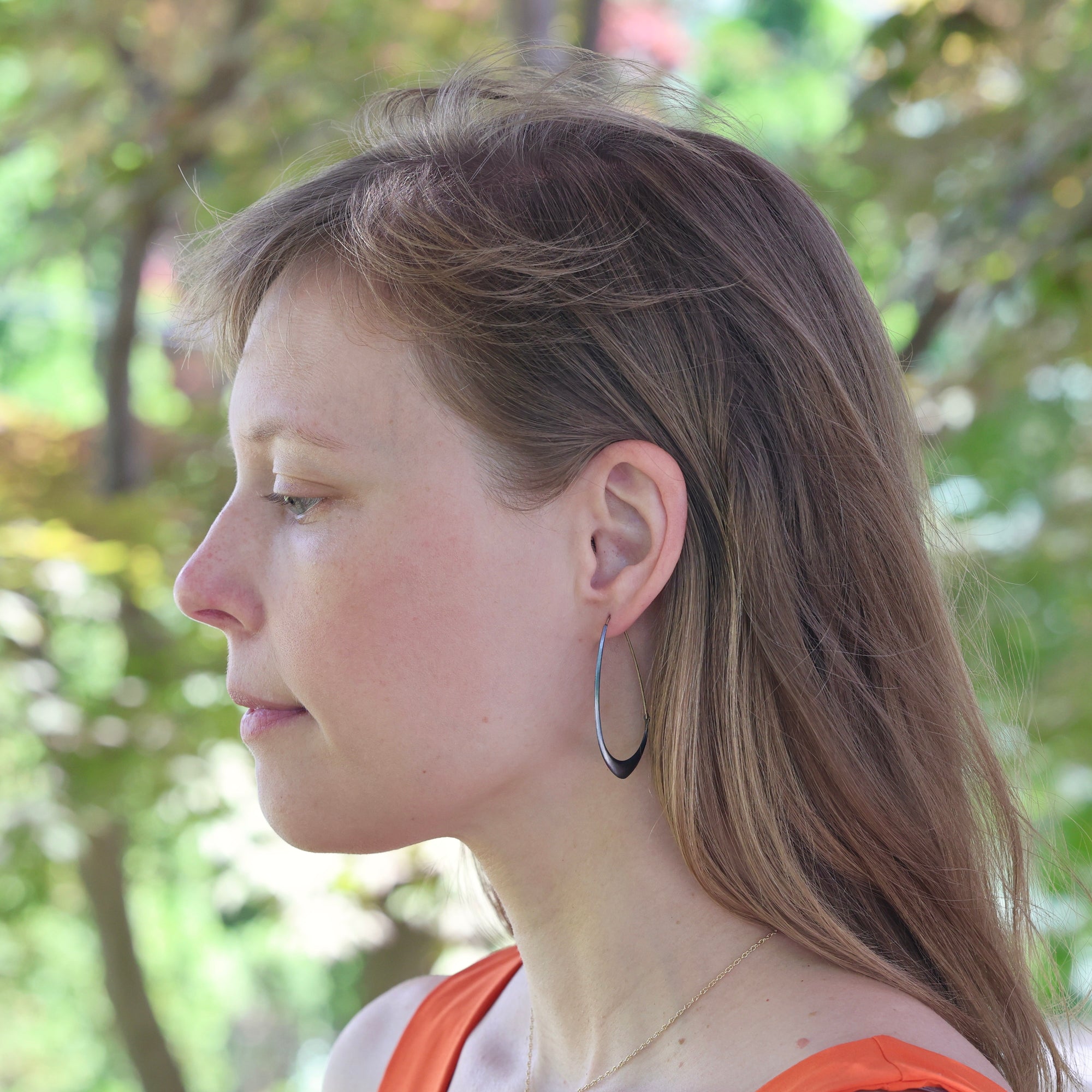 Woman with hoop earrings looking to the side with a blurred green background