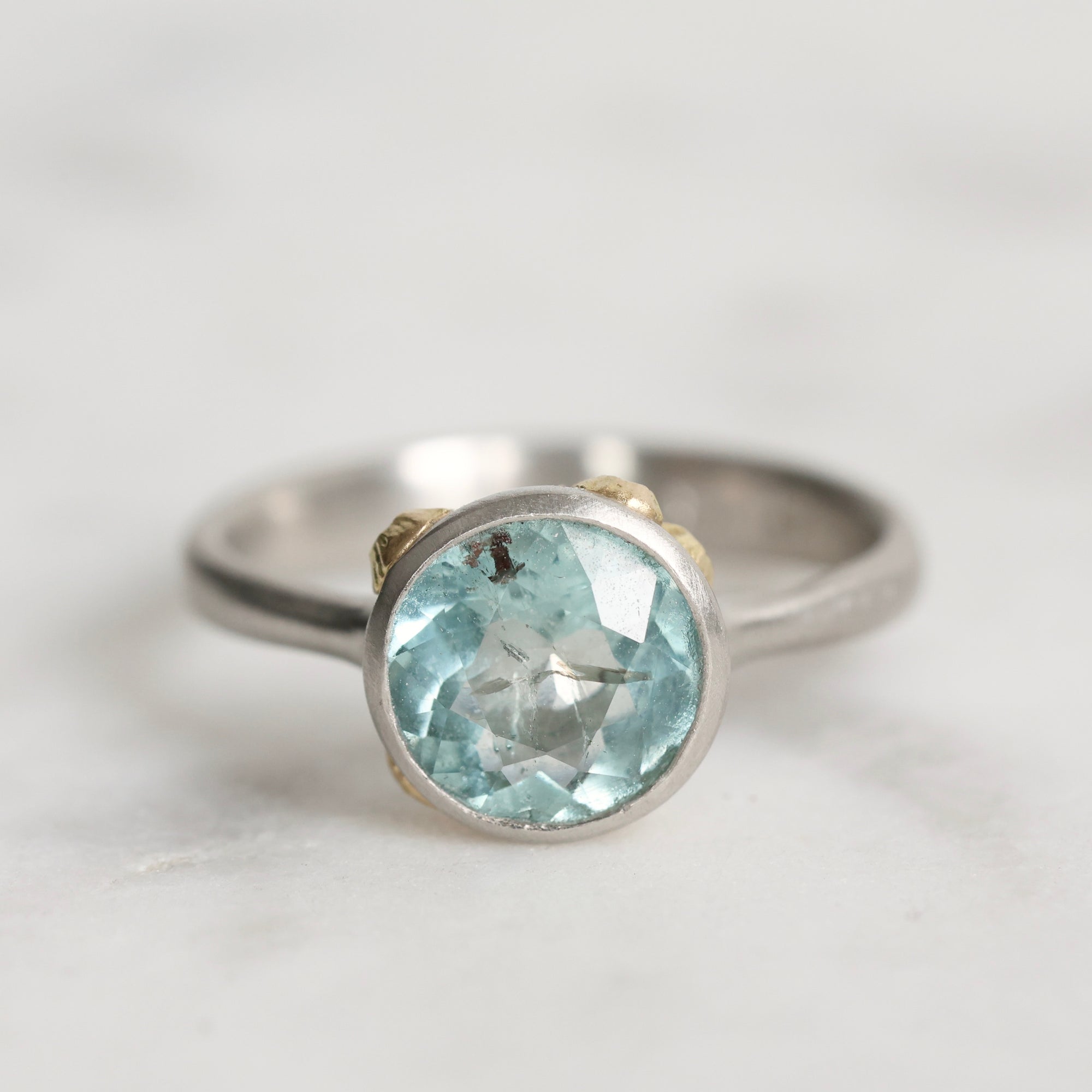 Silver ring with a light blue gemstone on a light gray background