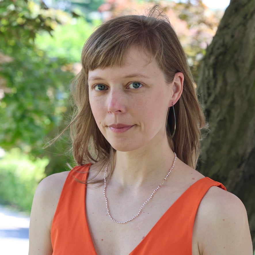 Woman with short hair wearing an orange top and necklace outdoors