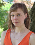 Woman with short hair wearing an orange top and necklace outdoors