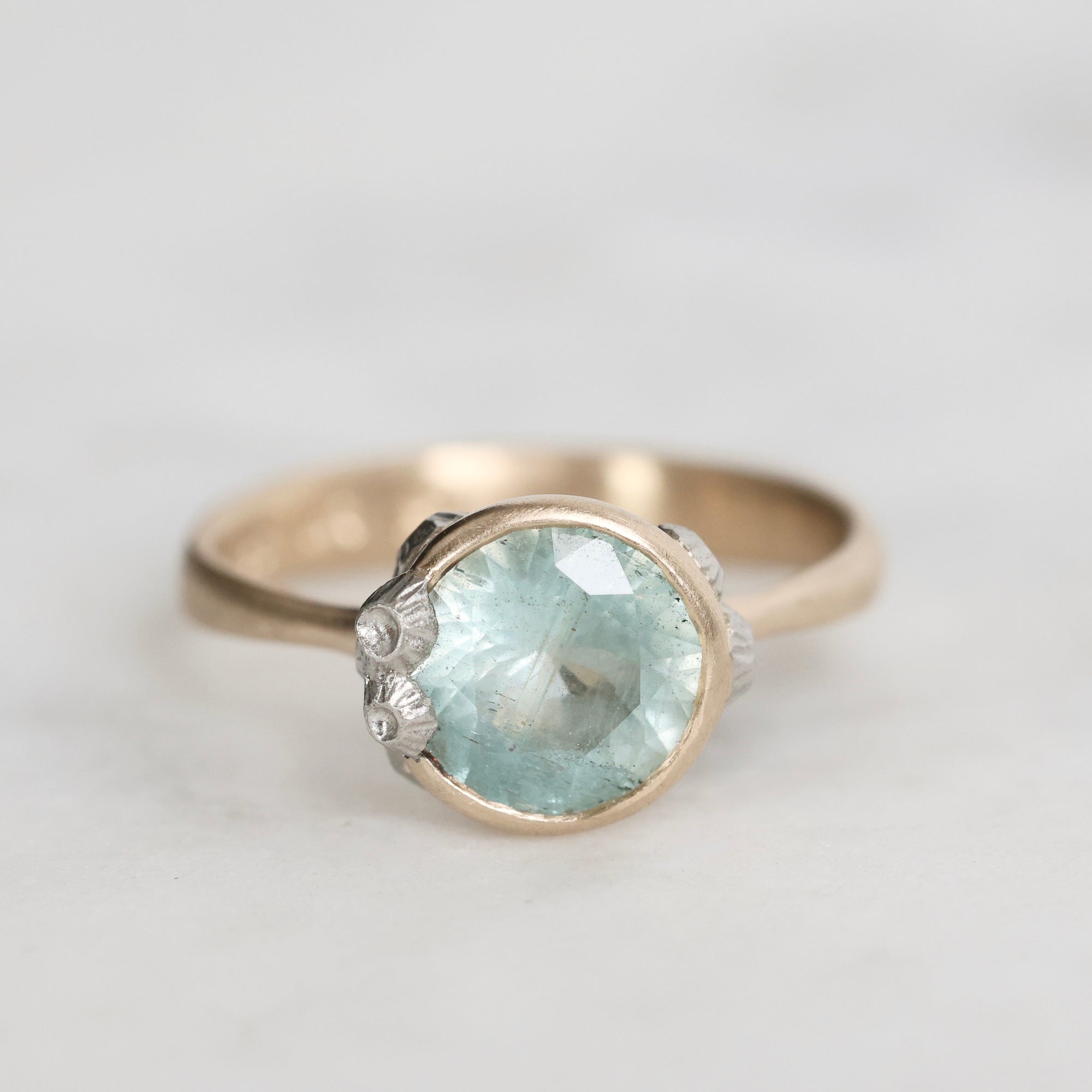 Gold ring with a large green gemstone on a light gray background