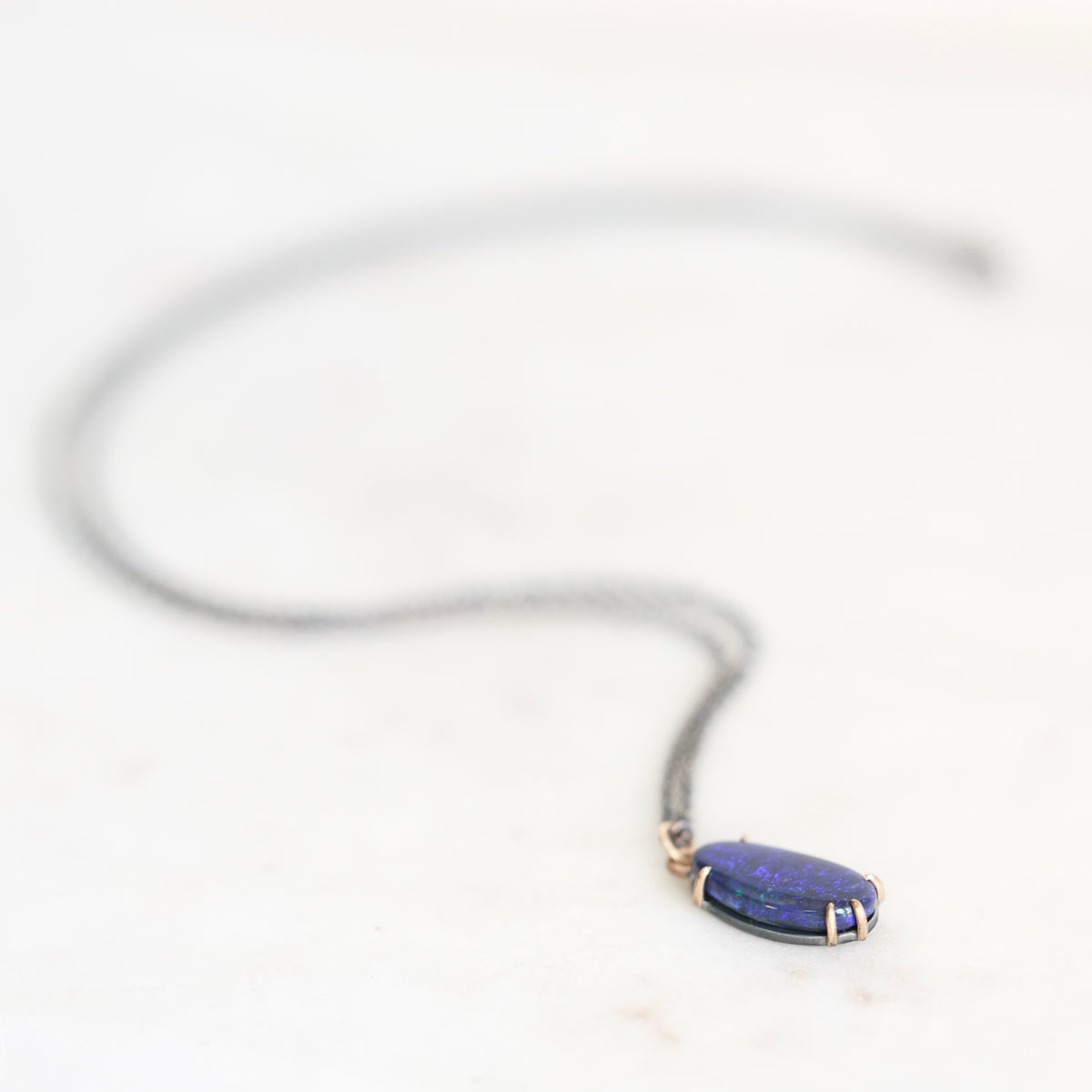 Opal necklace with gold prongs and oxidized silver chain laying on a marble background. 