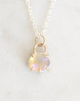 Light colored opal set in gold with a silver chain up close against a white marble background. 
