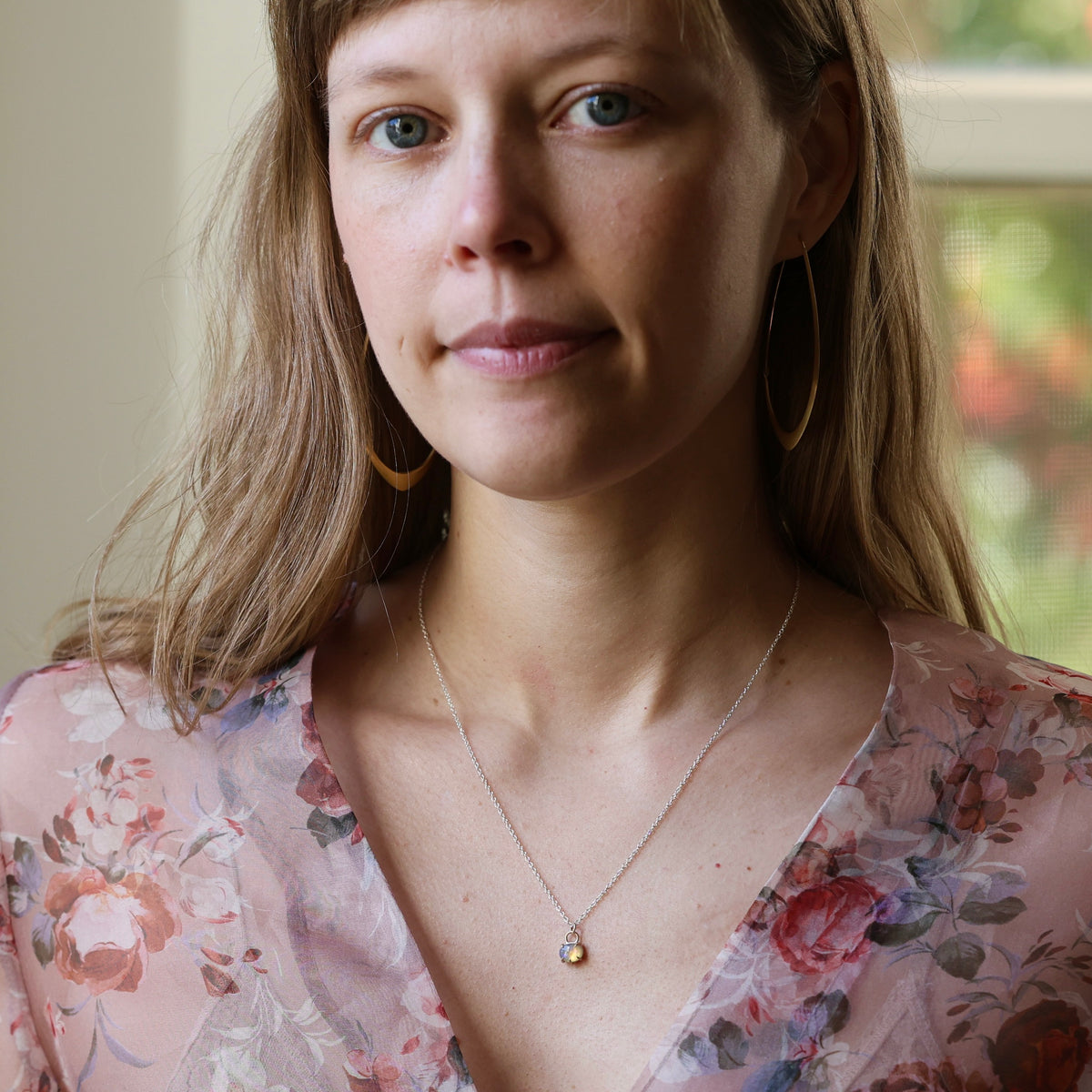 Woman wearing opal necklace and a floral blouse. She is looking at the camera, and set against an indoor background. 