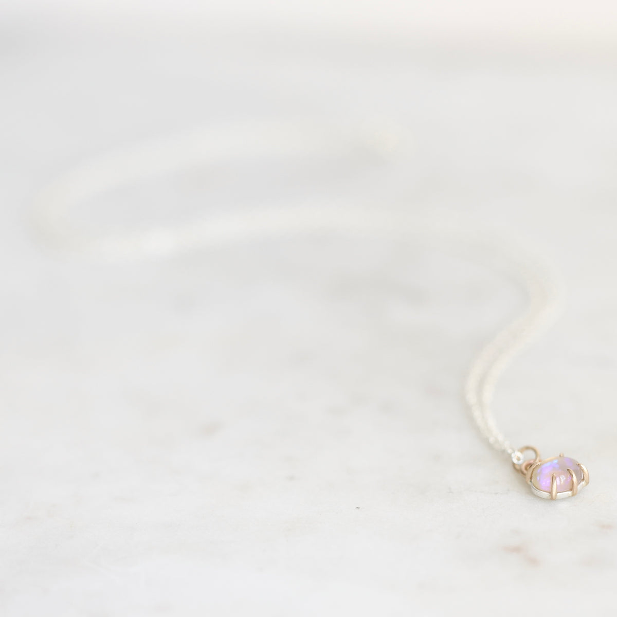 Light purple opal necklace with gold prongs and a silver chain against a plain marble background. 