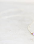 Light purple opal necklace with gold prongs and a silver chain against a plain marble background. 