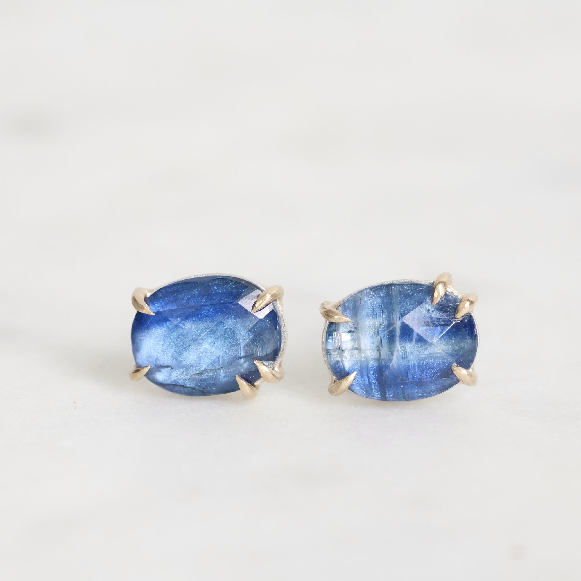 Pair of blue gemstone earrings with gold settings on a white background