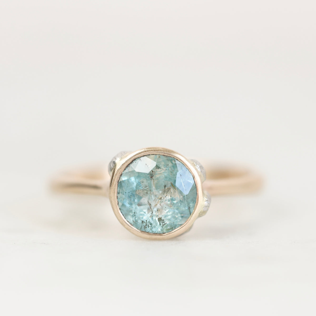 Blue bezel set gemstone ring with lots of inclusions against a plain background. 