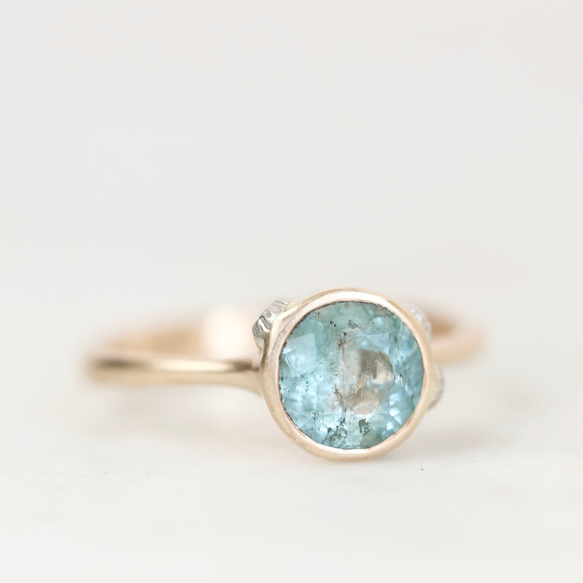 Blue gemstone bezel set ring with natural inclusions against a plain background. 
