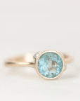 Blue gemstone bezel set ring with natural inclusions against a plain background. 
