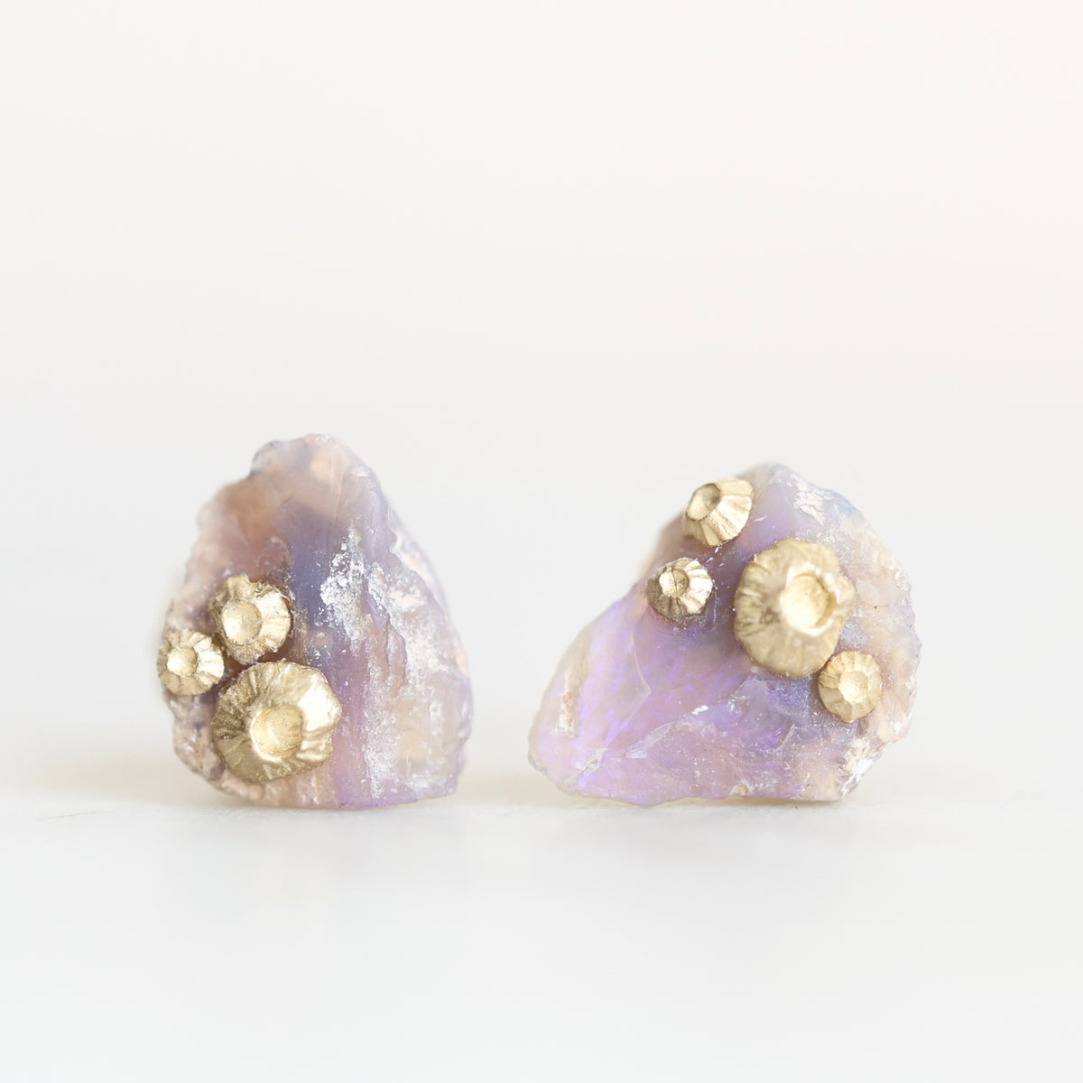 Raw opal studs with barnacle details in gold against a plain background. 