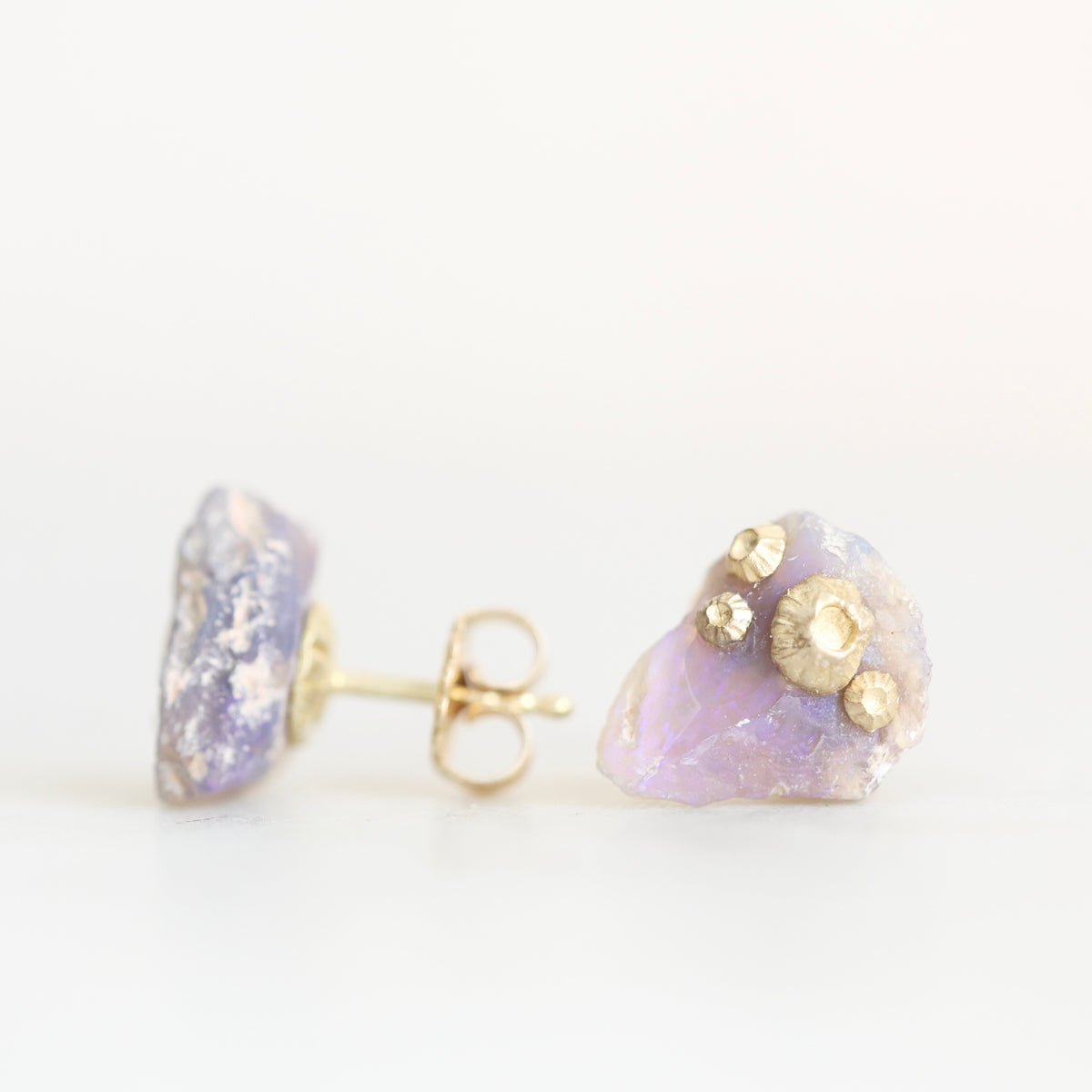 Raw opal studs with barnacle details in gold against a plain background. 