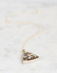 A silver-toned triangle pendant necklace with a textured, speckled brown and white pattern, suspended on a delicate gold-toned chain over a light marble background.