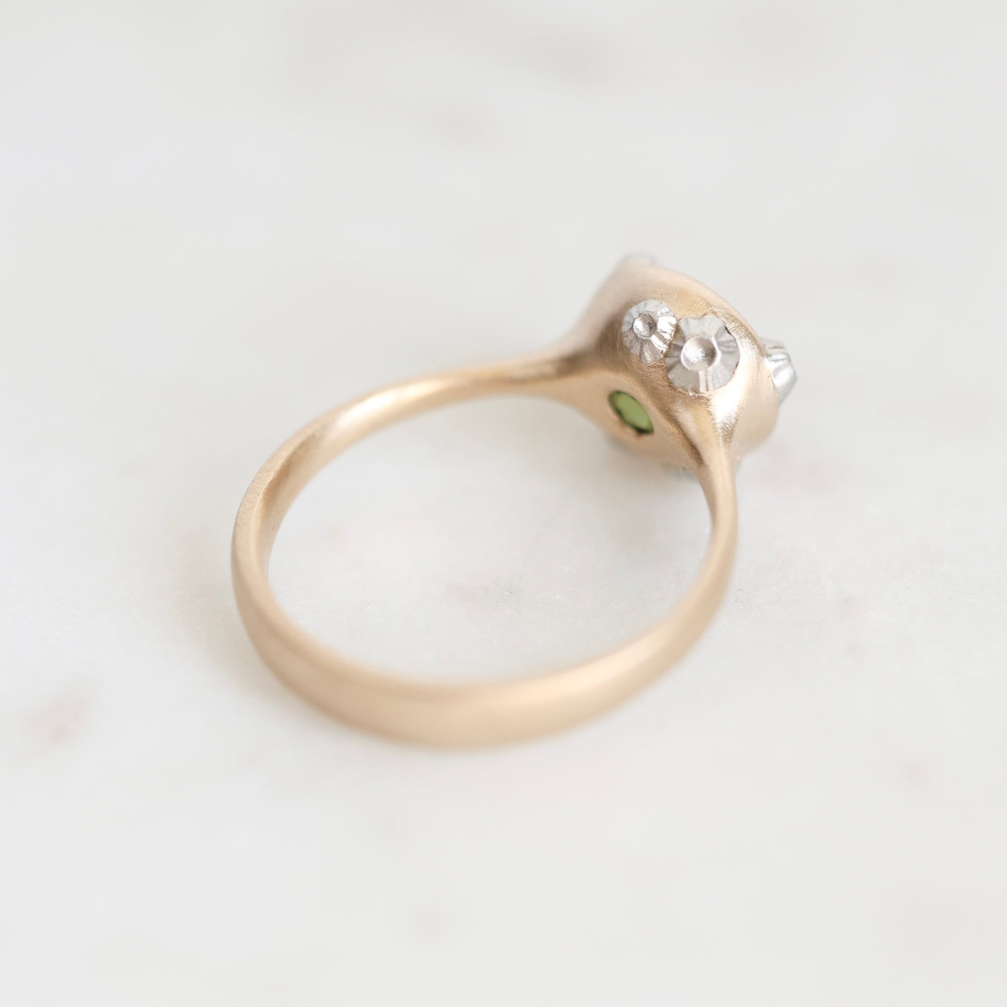 A vintage-style ring with a yellow gold band, a silver-toned setting, and small clear gemstones, photographed on a light marble surface.