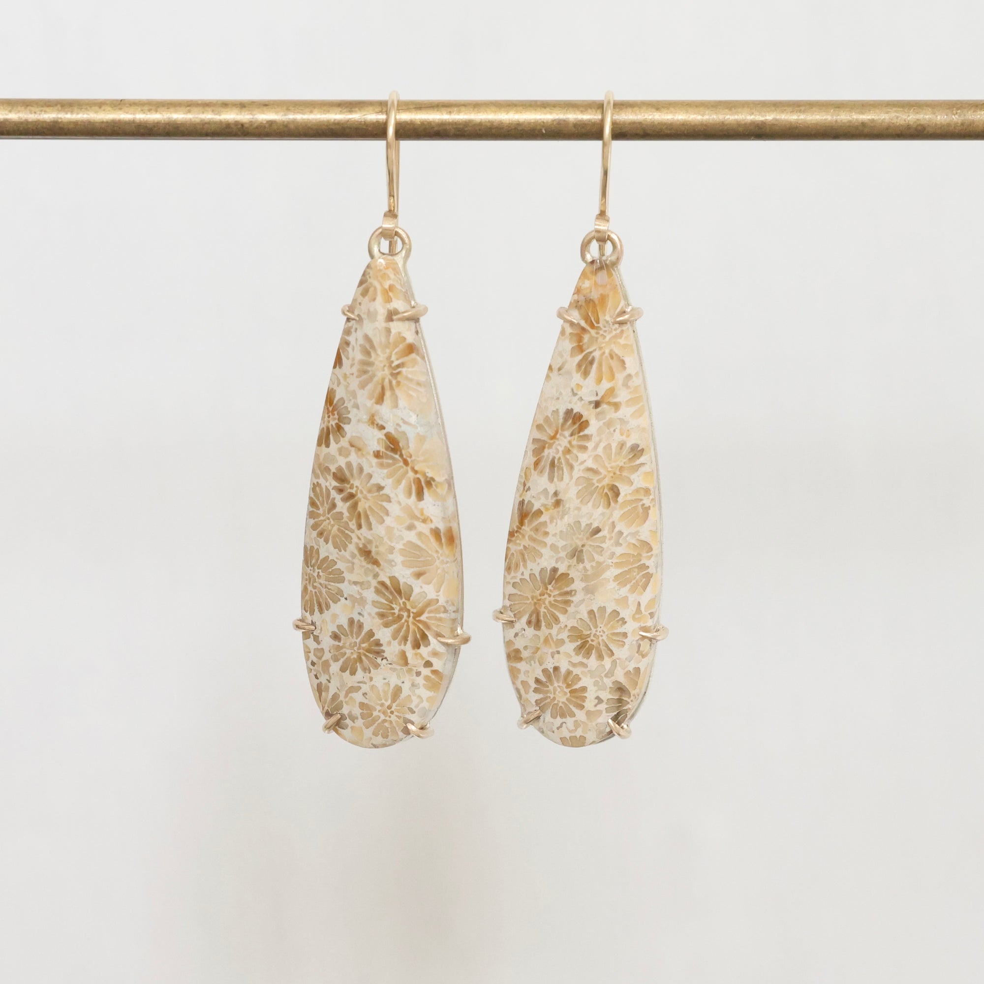 Pair of floral-patterned earrings on a gold rod against a light background