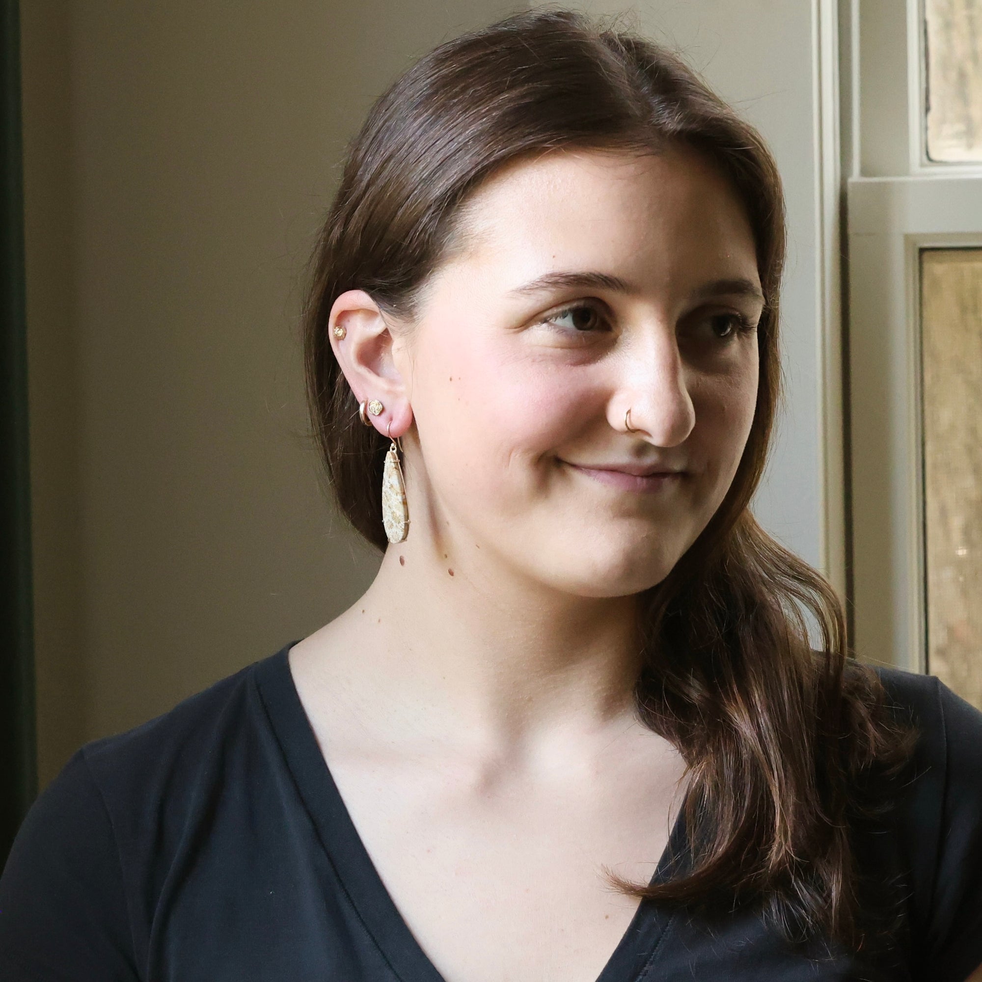 Woman with dark hair wearing earrings, smiling indoors.