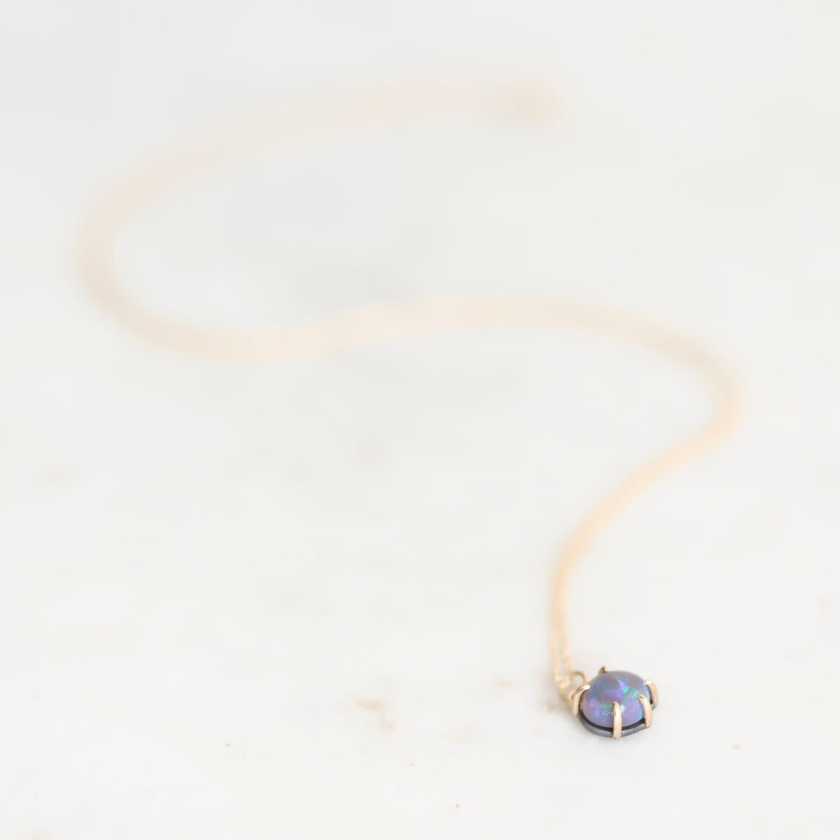 Opal necklace set in yellow gold with a yellow gold chain laying on a plain background. 